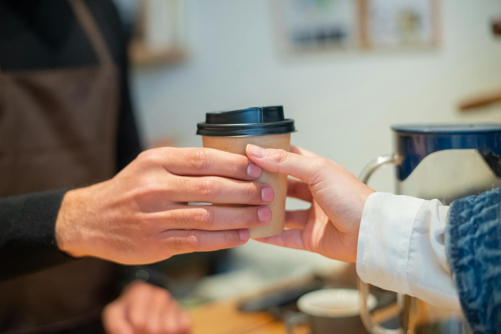 Close-up of barista handing a to-go coffee cup to a customer in a cozy cafe.